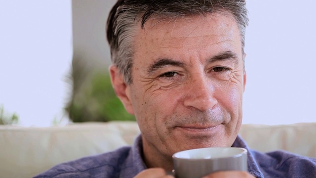一个快乐成熟的男人，坐在沙发上休息，在客厅喝着咖啡视频素材