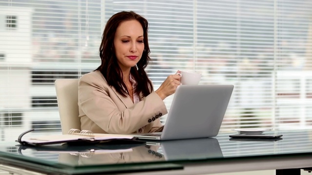 女商人一边喝咖啡一边在笔记本电脑上打字视频素材