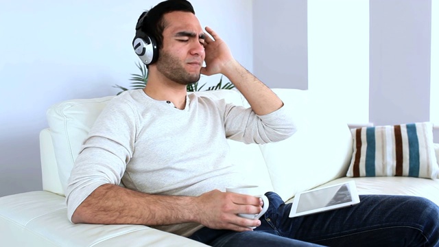 一名男子坐在沙发上用平板电脑听着音乐视频素材