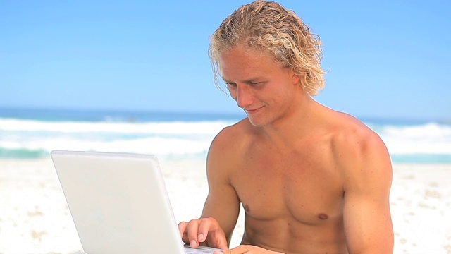 快乐的金发男人拿着他的笔记本电脑在海滩上视频下载