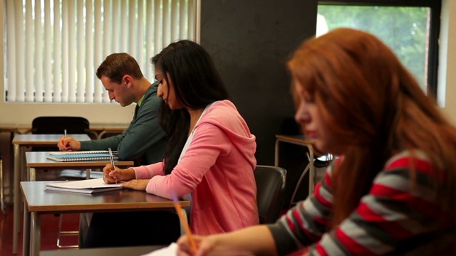 在大学里，专注的学生坐在教室里做笔记视频素材