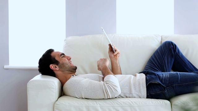 躺在沙发上的男人在用平板电脑视频素材
