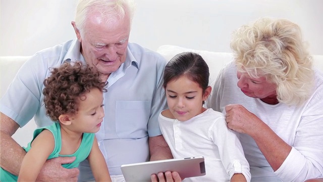两个祖父母和两个孩子在用平板电脑视频素材