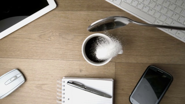 慢镜头里，一茶匙的糖粉洒在了一张办公桌上的一杯咖啡周围视频下载