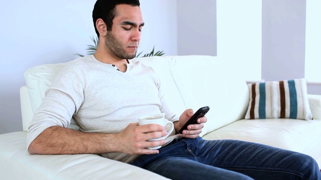一个男人一边喝咖啡一边用笔记本电脑和智能手机视频下载
