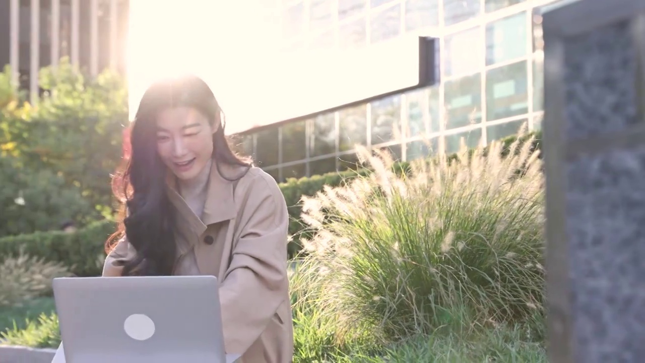 高知商务女子坐在户外办公园区使用笔记本电脑视频工作，欢呼庆祝成功视频素材