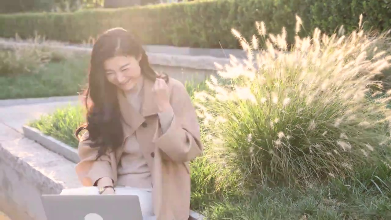 高知商务女子坐在户外办公园区使用笔记本电脑视频工作，欢呼庆祝成功视频下载
