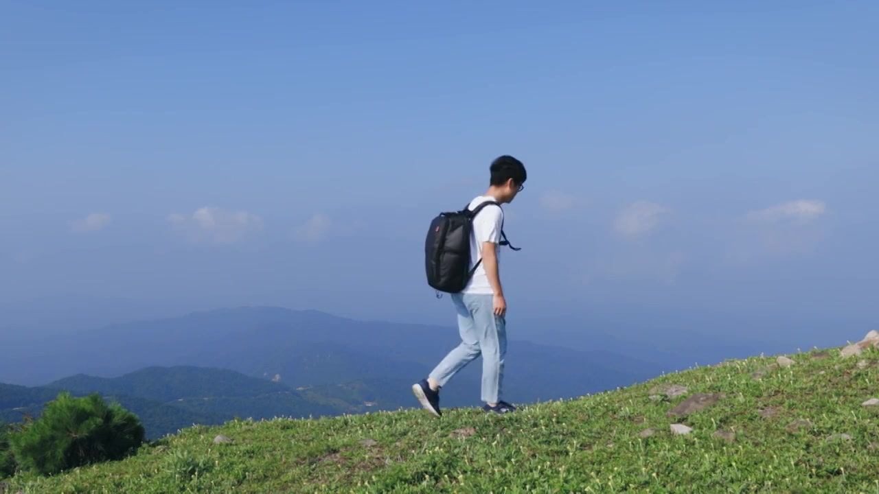 4K一个年轻男性背包在山顶上行走观看风景视频素材