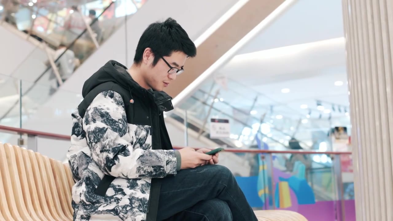 4K年轻男性在商场坐着休息玩手机特写视频下载