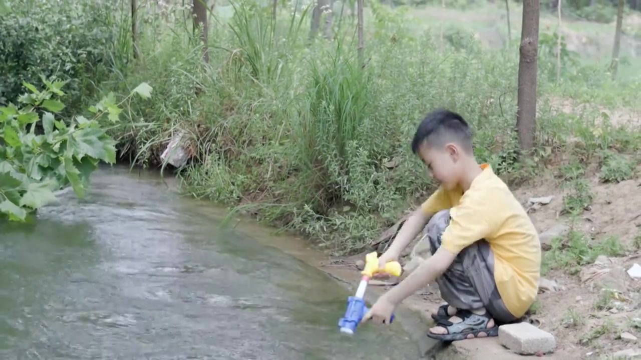 4K一个小男孩在小溪边玩水枪视频下载