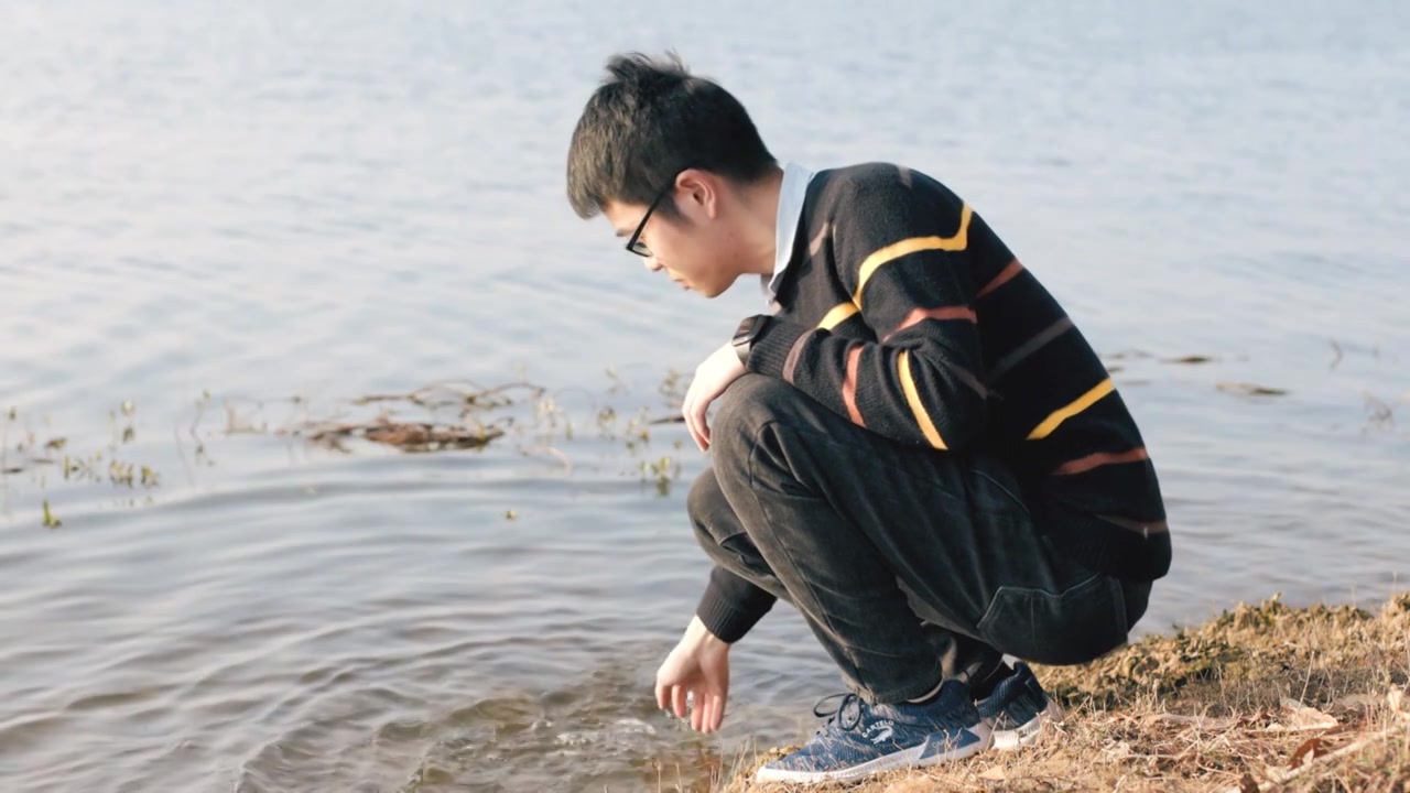 4K年轻男性在湖边拨动水花视频素材