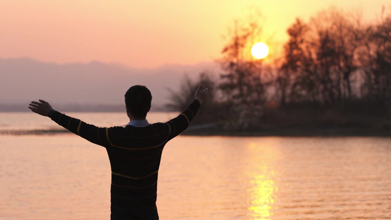 4K日落时分湖边的年轻男性举起双手视频素材