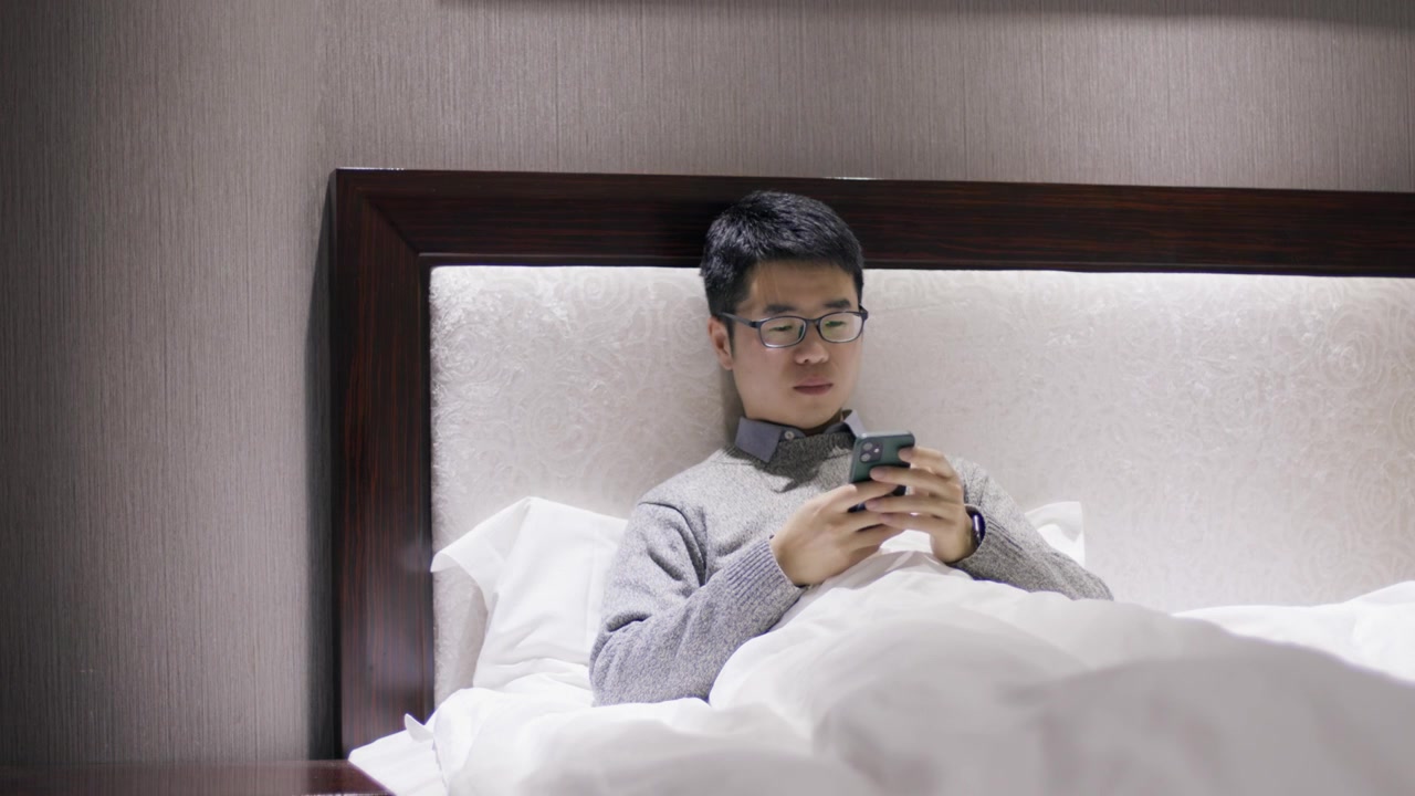4K年轻男性出差在酒店床上躺着玩手机视频下载