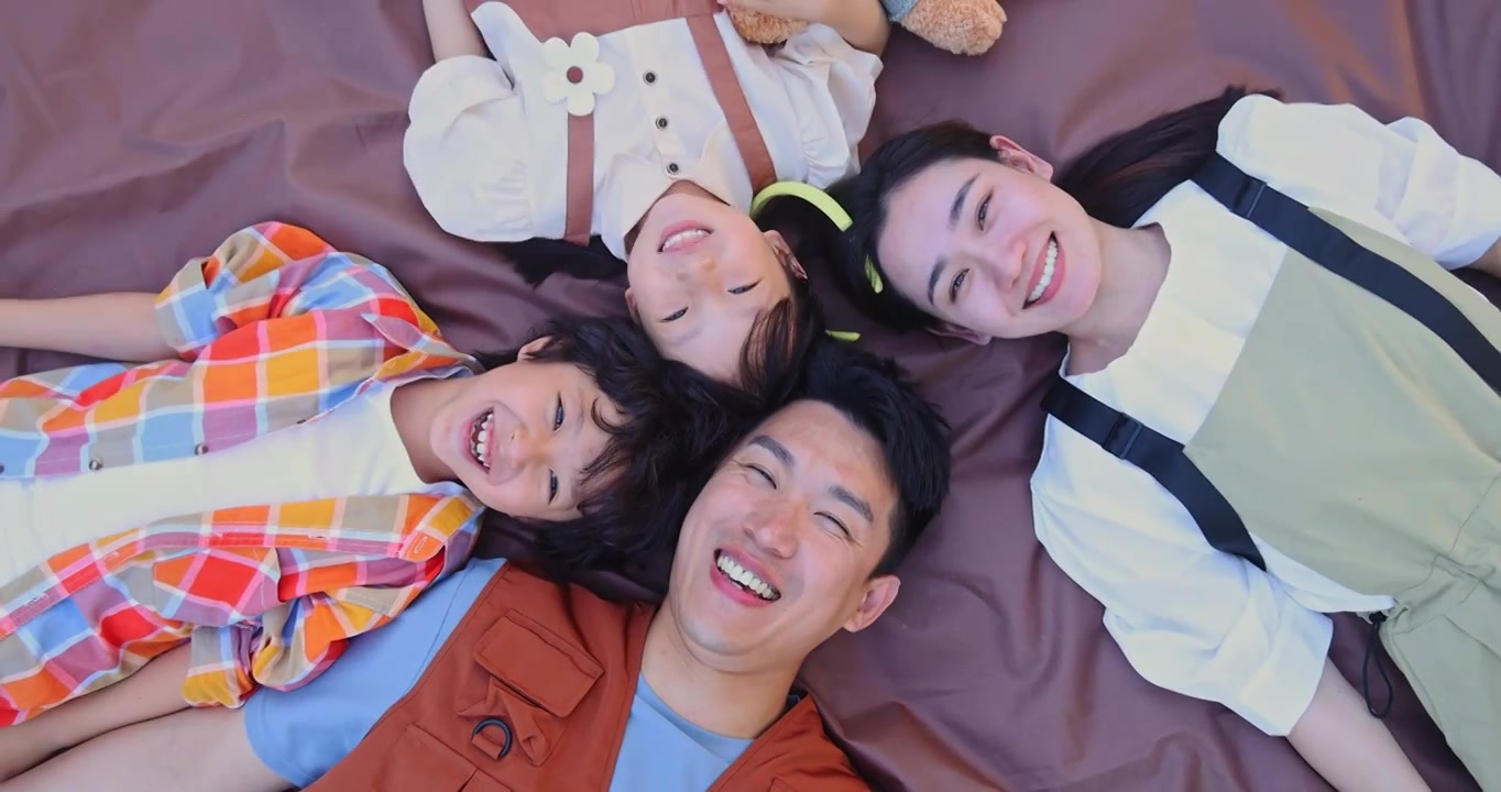 一家四口躺在野餐垫上微笑看镜头视频下载