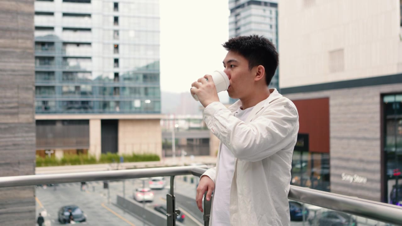 在一个阴天，一位男商人在公司外的阳台上休息——下班后喝一杯咖啡，促进健康，工作与生活的平衡视频下载