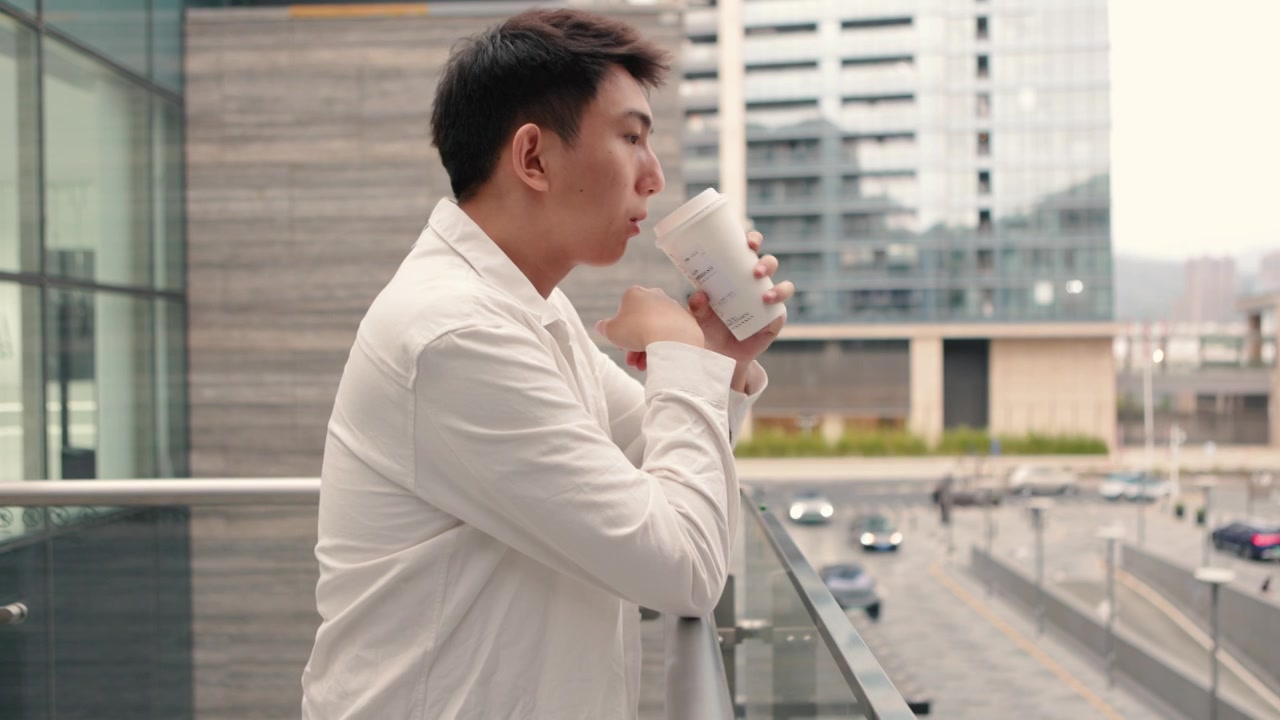 在一个阴天，一位男商人在公司外的阳台上休息——下班后喝一杯咖啡，促进健康，工作与生活的平衡视频素材