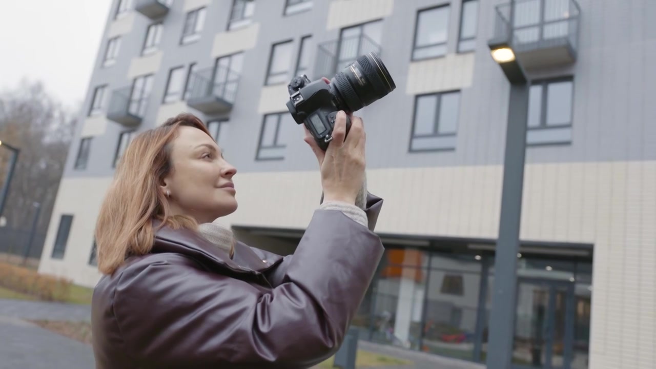 女子用专业相机在建筑物的背景下拍照。行动视频下载