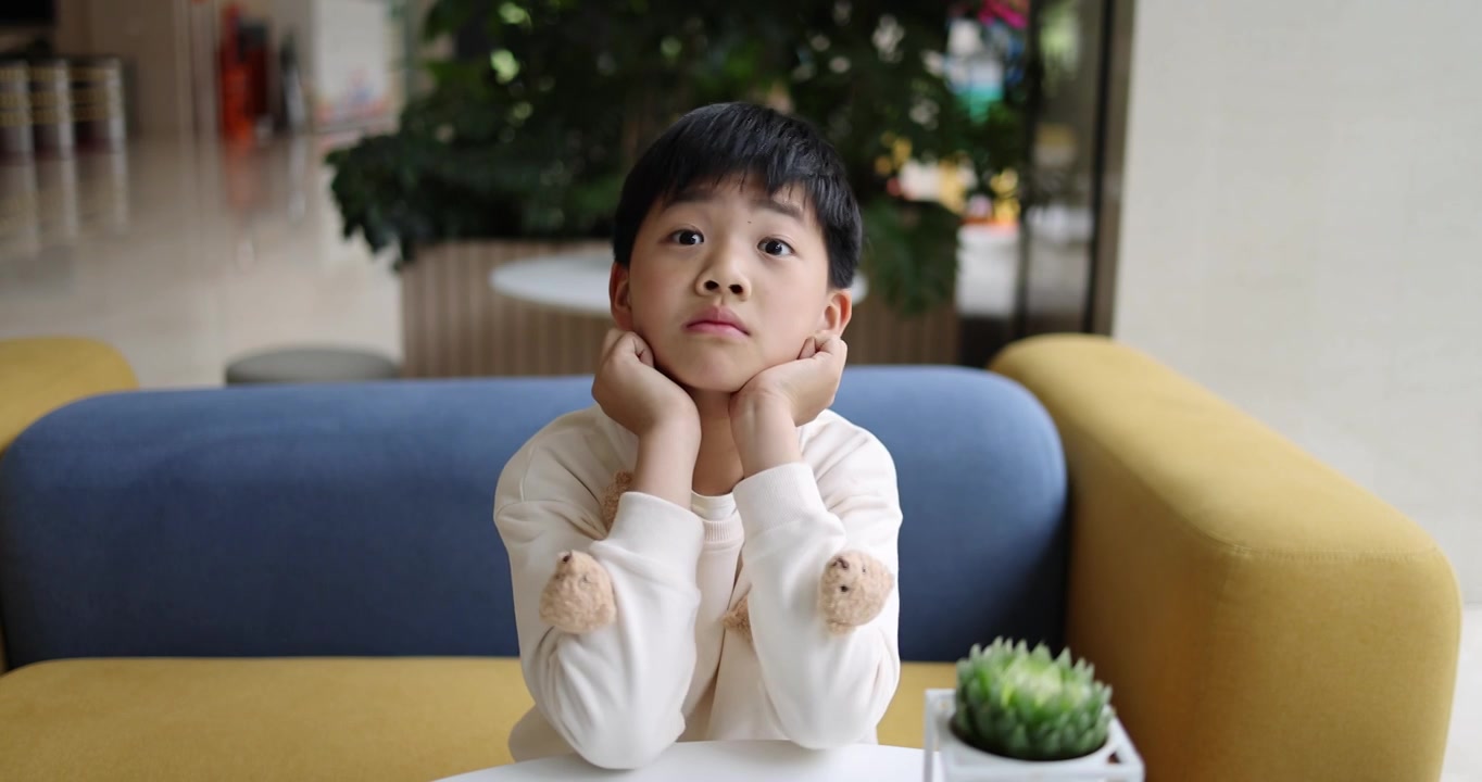 可爱的中国小男孩坐在沙发上托腮卖萌视频素材