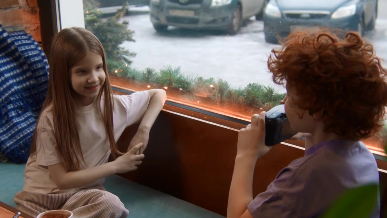 一个红卷发男孩在旁边的咖啡馆给一个可爱的长发女孩拍照视频下载