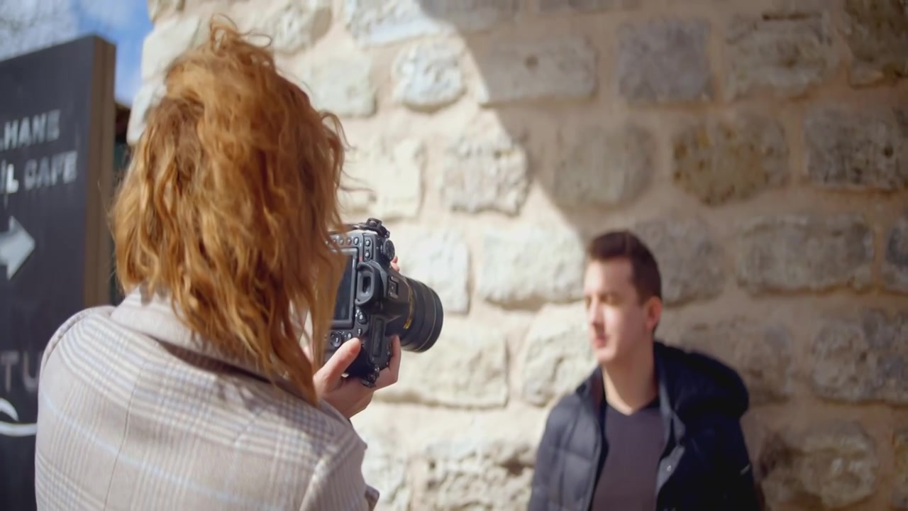 一个女人在墙前给一个男人拍照。行动。红发女人视频下载
