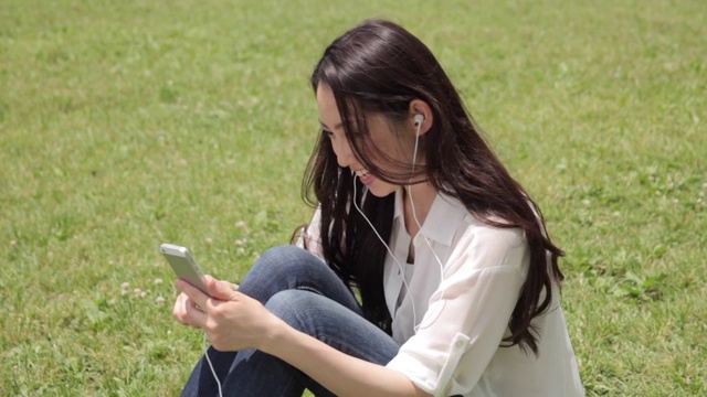 迷人的年轻日本女人在城市公园听音乐视频素材
