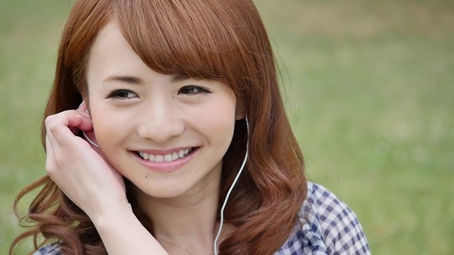 年轻迷人的日本女子在城市公园听音乐视频下载