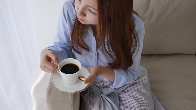 一个年轻的日本女人在沙发上喝咖啡视频素材