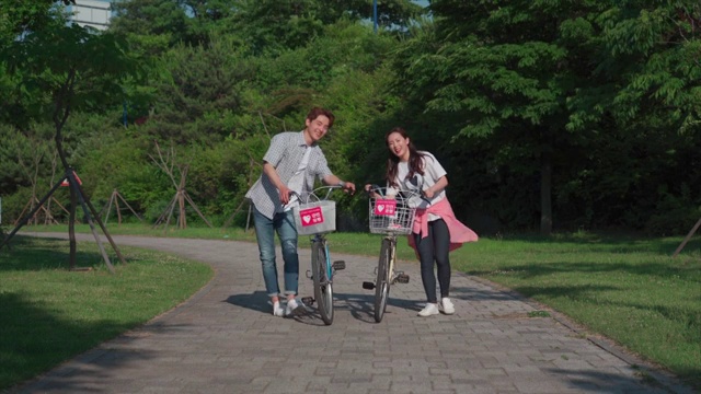 这对年轻夫妇在公园里推着一辆自行车视频素材