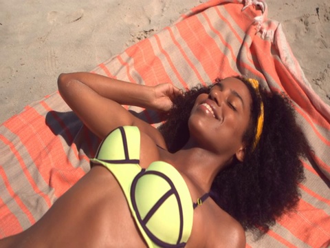 美丽年轻的非洲裔美国妇女在绿色比基尼放松在毯子在海滩视频下载