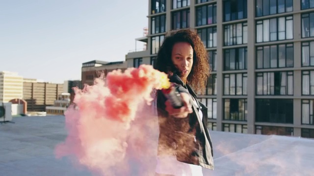 时尚的年轻女子在城市的屋顶上使用烟雾弹视频素材