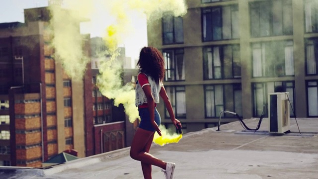 时尚的年轻女子在城市的屋顶上使用烟雾弹视频素材
