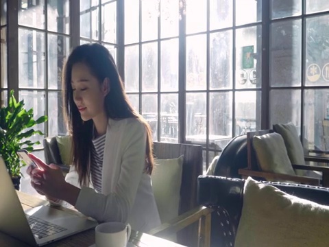 年轻商务女士在咖啡店使用手机视频下载