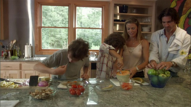 中等镜头的女人帮男孩舀哈密瓜，其他男孩在厨房给父亲吃煎蛋卷视频下载