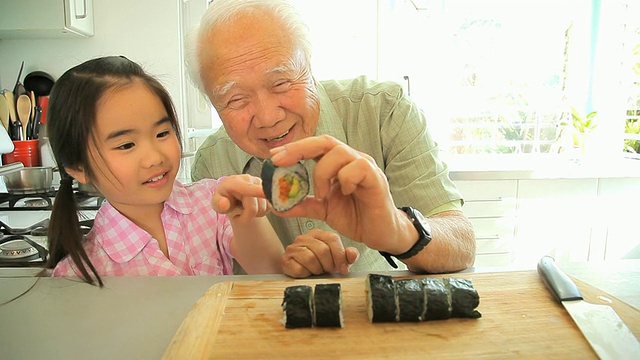 美国加州洛杉矶，祖父向孙女(8-9)演示如何切寿司卷视频下载