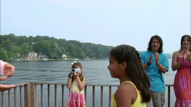 男人和女孩在屋顶上跳舞，在派对上俯瞰湖，而女孩用数码摄像机/新泽西电影视频素材
