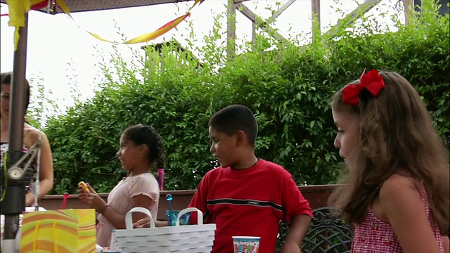 在生日派对上，成年人和孩子们围着伞坐着/男人用数码摄像机拍摄家庭电影，女人端着冰淇淋/新泽西视频素材