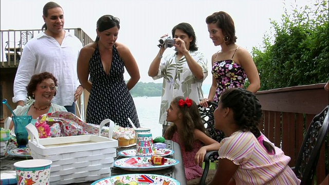 在她的生日聚会上，当男人用数码摄像机拍摄家庭电影时，女人给年轻的女孩作为礼物视频素材