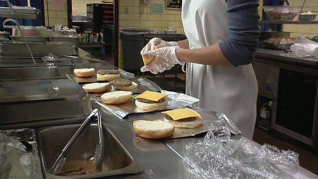 美国密歇根州贝尔维尔市，库克女士在学校厨房准备芝士片汉堡视频素材