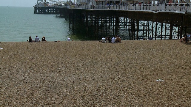英国布莱顿，人们坐在面对布莱顿码头的卵石海滩上视频下载