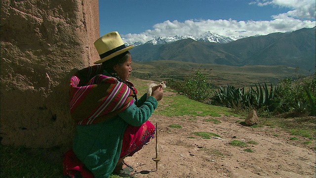 秘鲁库斯科地区山区的一名秘鲁妇女穿着色彩鲜艳的衣服，用纺锤来纺线视频下载