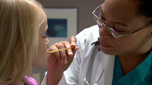 医生把体温计放进小女孩的嘴里，然后走开视频素材