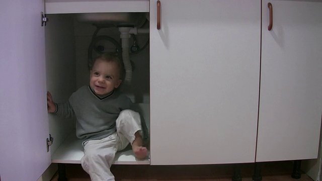 小男孩在厨房的橱柜里玩耍视频素材