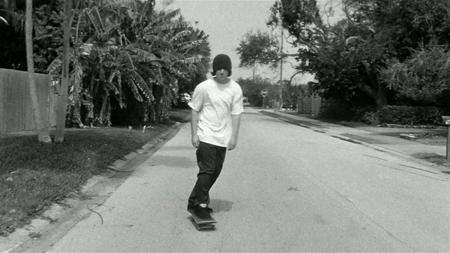 一个年轻人在住宅区的街道上滑冰，拐过一个拐角，然后滑上了路缘视频下载