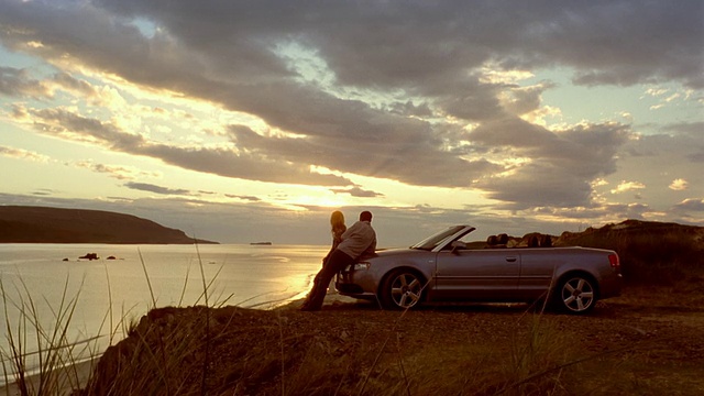 一对夫妇靠在停在悬崖上的敞篷车上，看着夕阳下的湖/拥抱/苏格兰视频下载
