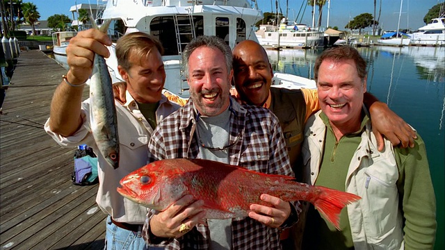 四名男子在码头上微笑着举着他们的鱼/长滩，加利福尼亚视频下载