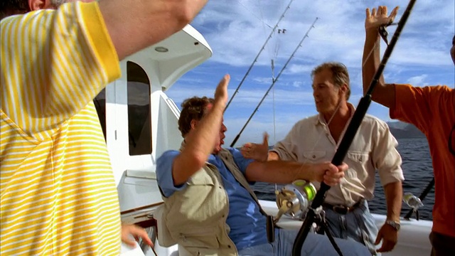 中拍摄坐在游艇上的战斗椅上，与鱼在他的线挣扎，他的朋友包围他/人在网/加州捞红鲷鱼视频下载