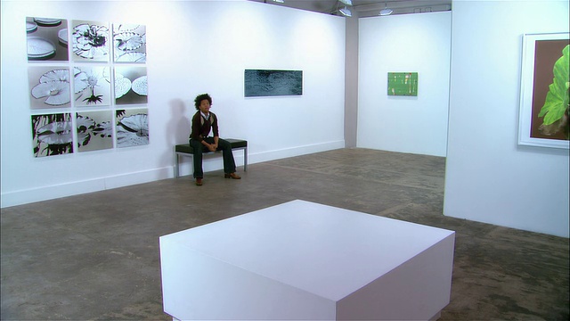 一个年轻人坐在画廊的长凳上视频下载