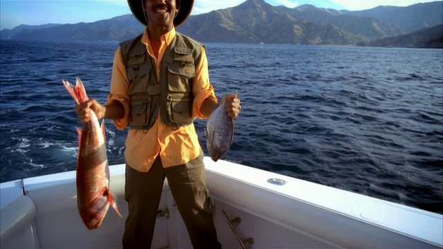 一名中枪男子微笑着举着鱼在渔船上/加州长滩视频下载