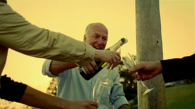 一名老人打开一瓶香槟/香槟从瓶中流出，男子将香槟倒进四人用的笛子里视频素材