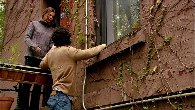 中镜头倾斜的男人在梯子上工作窗户/女人给男人端咖啡/布鲁克林，纽约视频下载